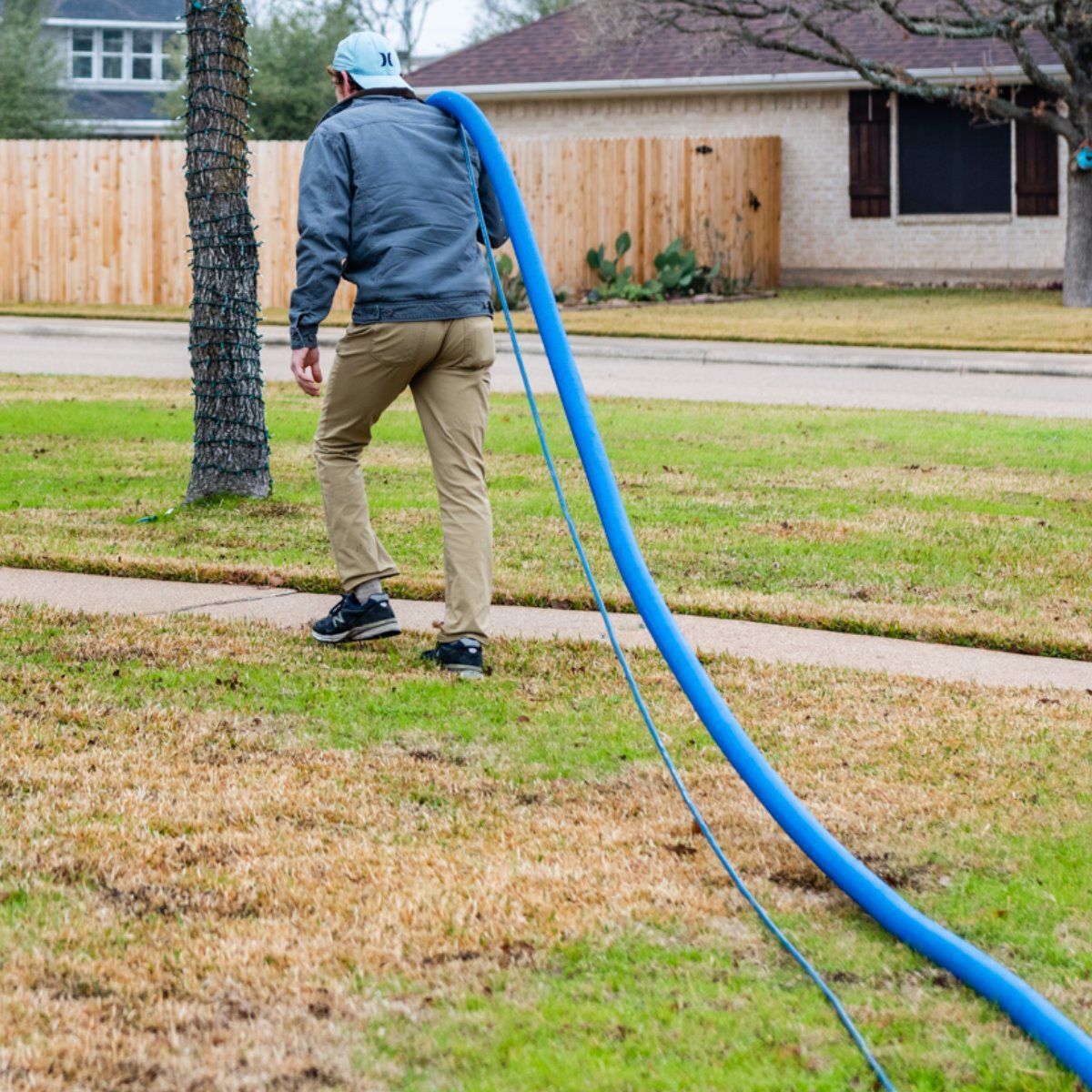 a man is walking down a sidewalk with a blue hose attached to him .