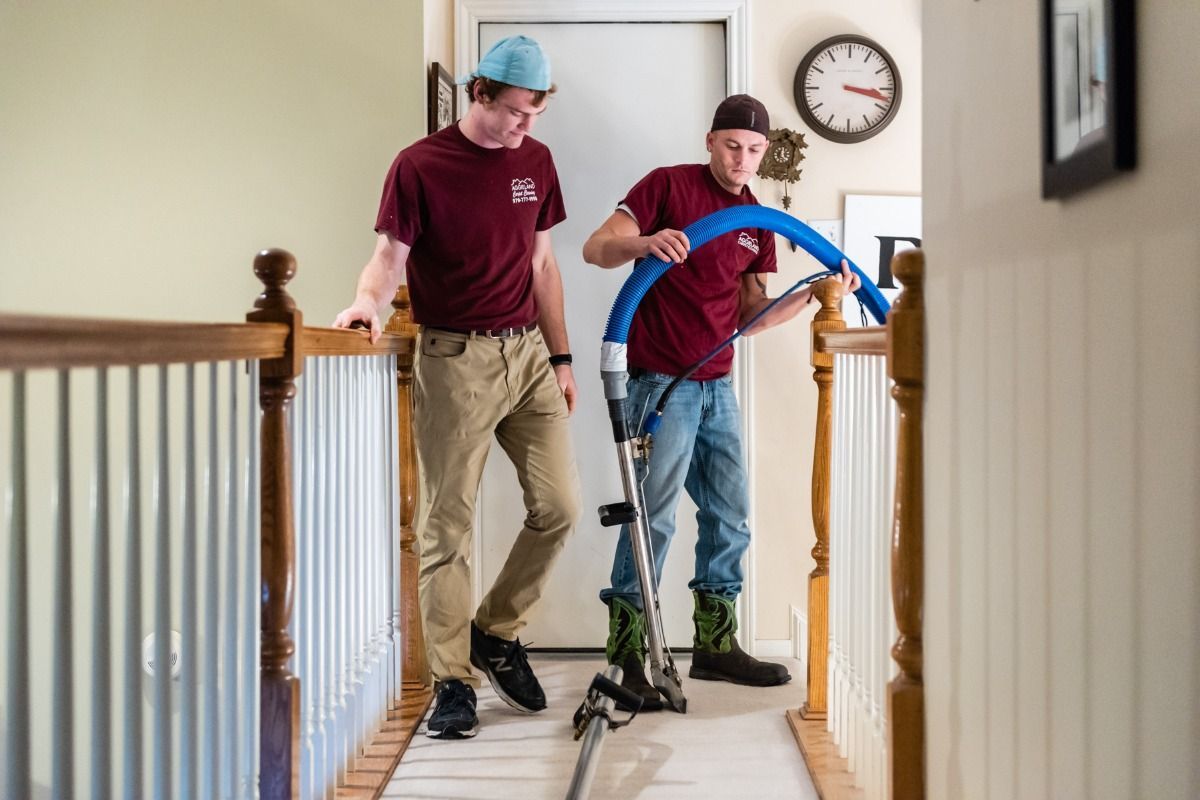 two men are cleaning a hallway with a vacuum cleaner .