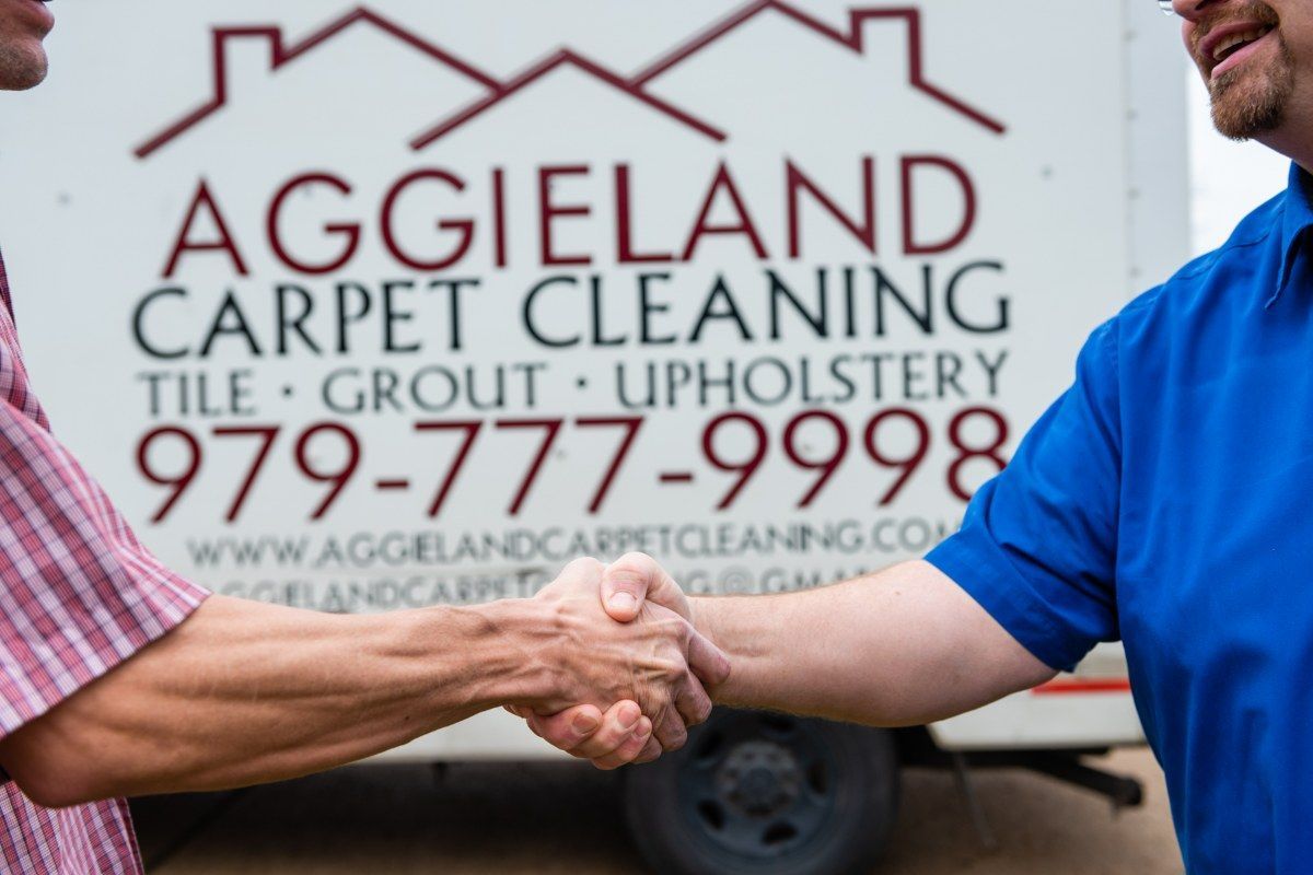 two men shaking hands in front of an aggieland carpet cleaning truck