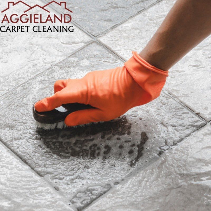 a person wearing orange gloves is cleaning a tile floor with a brush