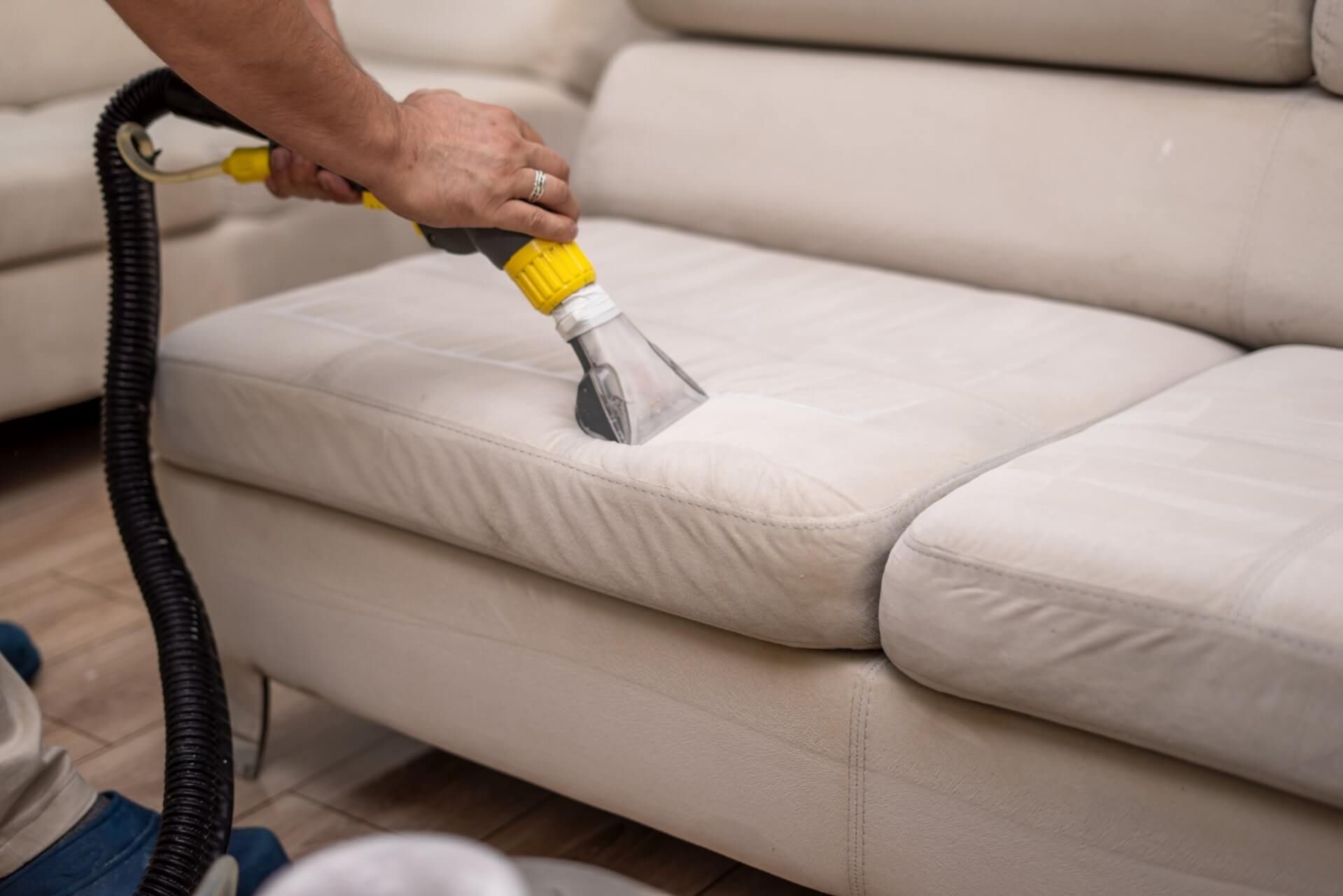 a person is cleaning a white leather couch with a vacuum cleaner .