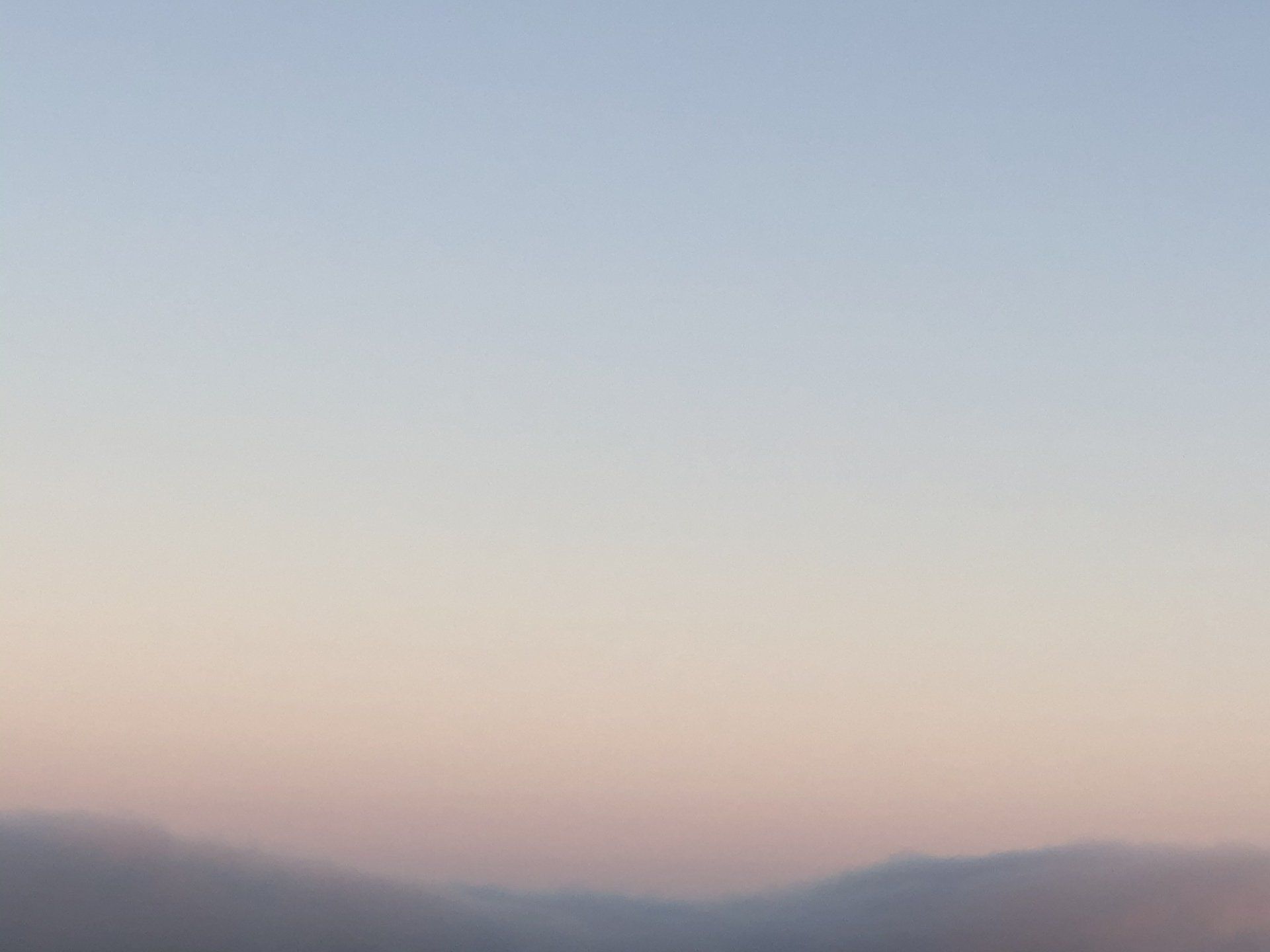 A sunset with mountains in the foreground and a blue sky in the background.