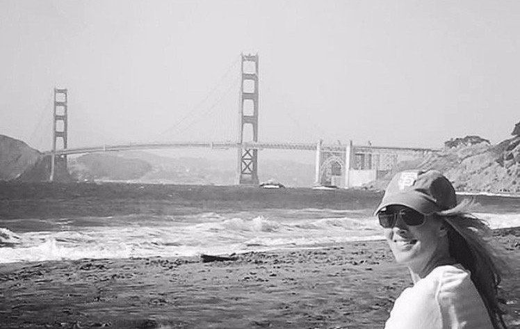 A woman is standing on a beach in front of the golden gate bridge