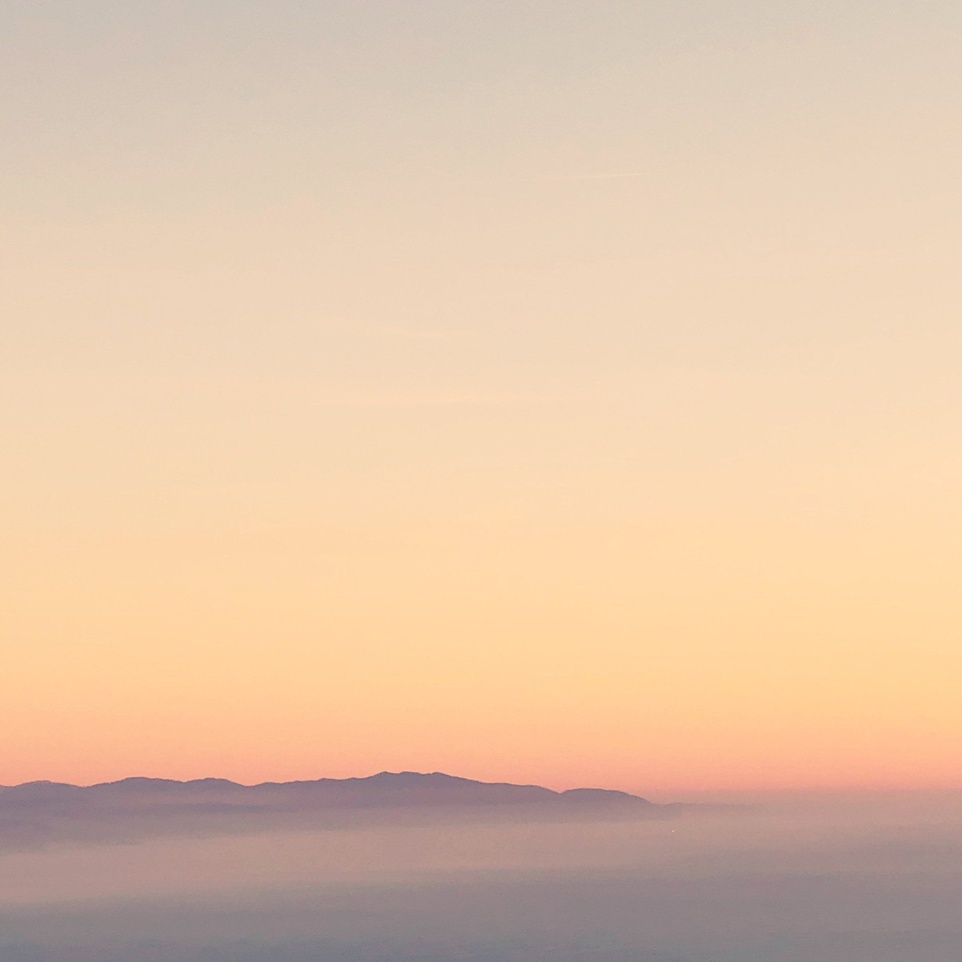A sunset over a foggy valley with mountains in the distance.