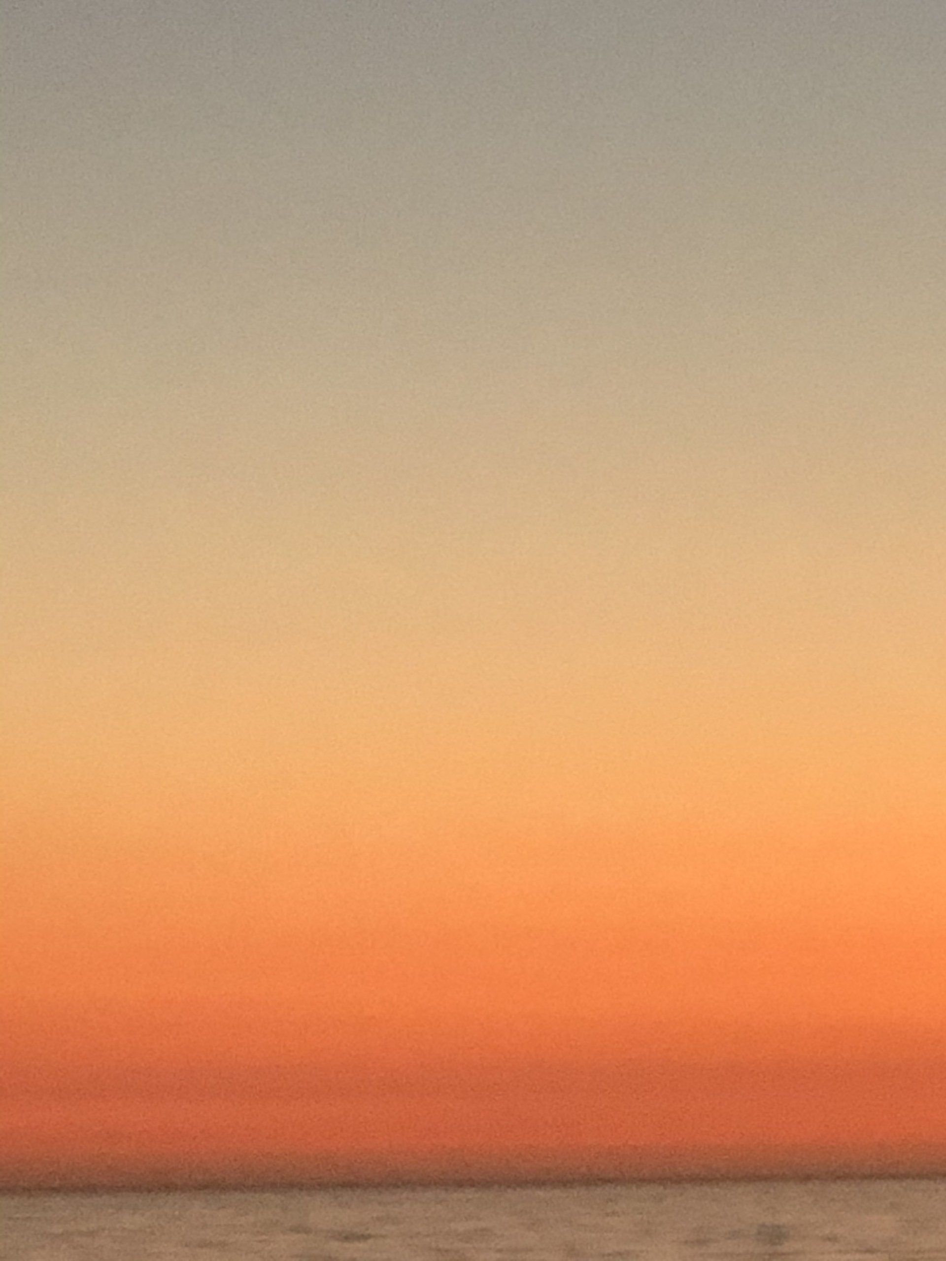 A sunset over the ocean with a gradient of orange and gray.