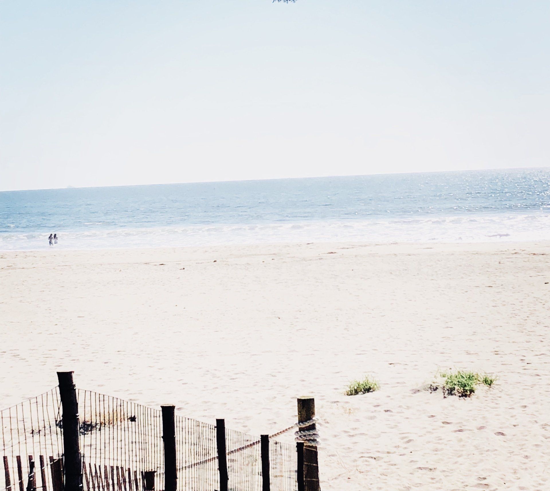 A beach with a fence in the foreground and the ocean in the background