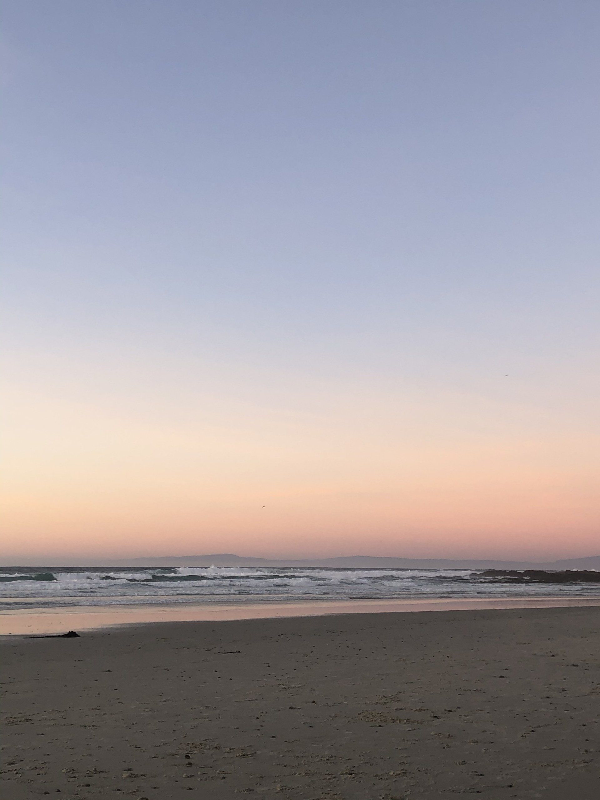 A beach with a sunset in the background and waves crashing on the shore.