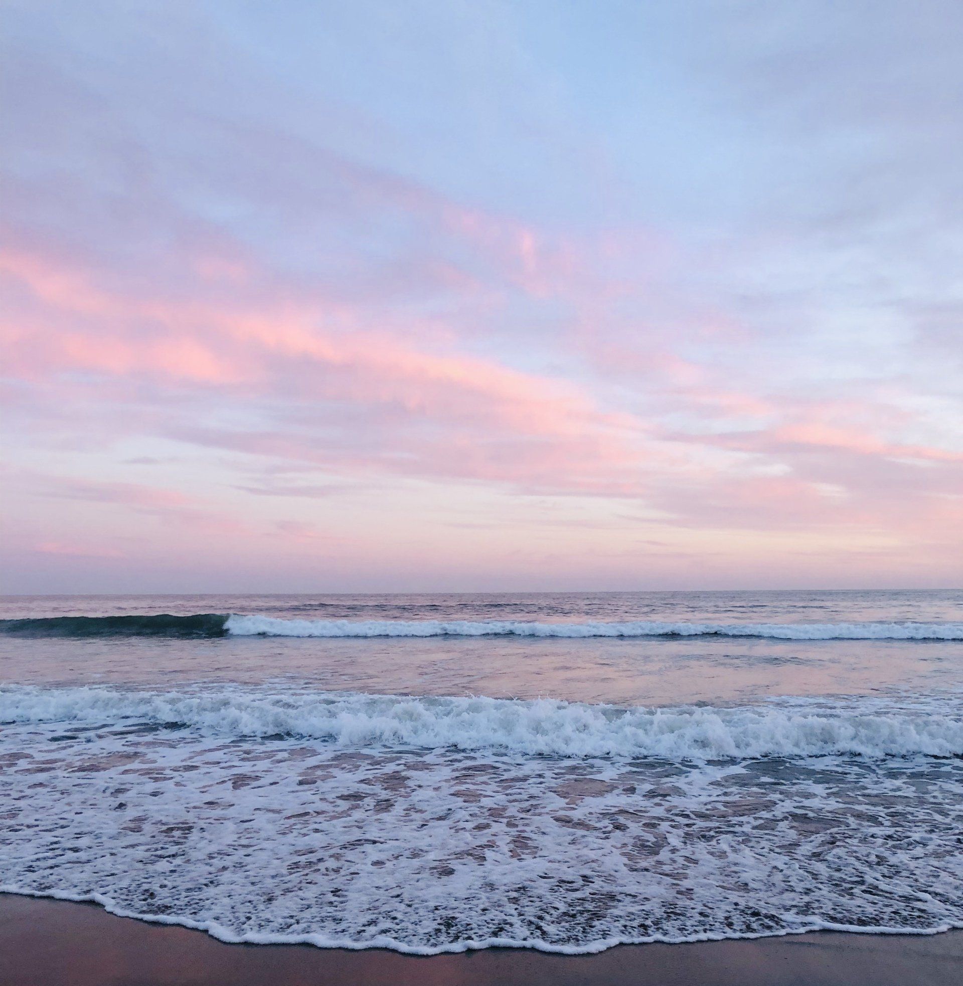 A beach with waves crashing on the sand at sunset
