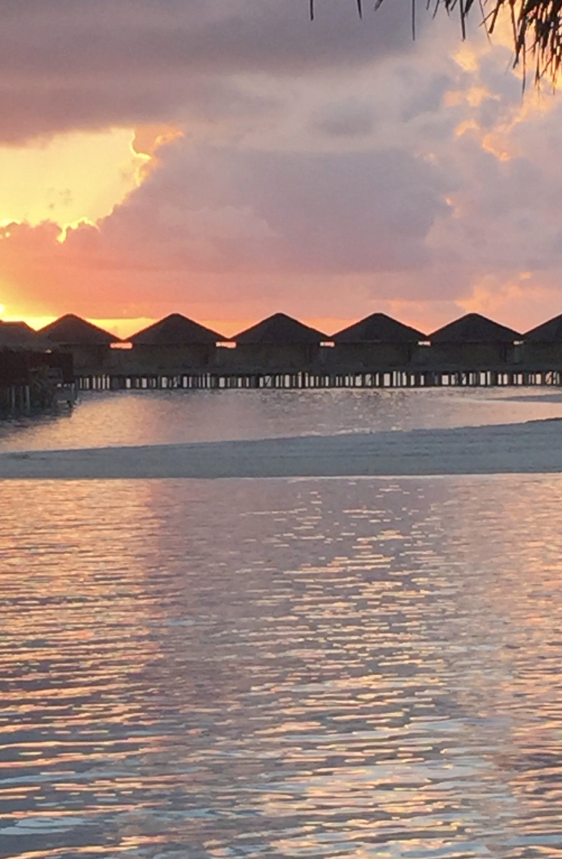 A sunset over a body of water with a row of bungalows in the background