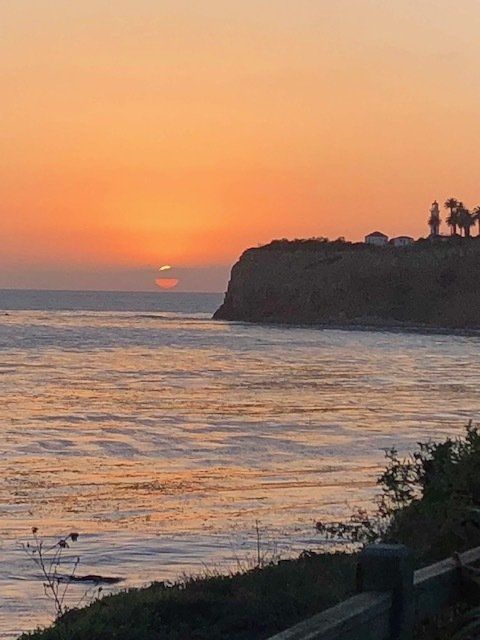 A sunset over the ocean with a cliff in the foreground