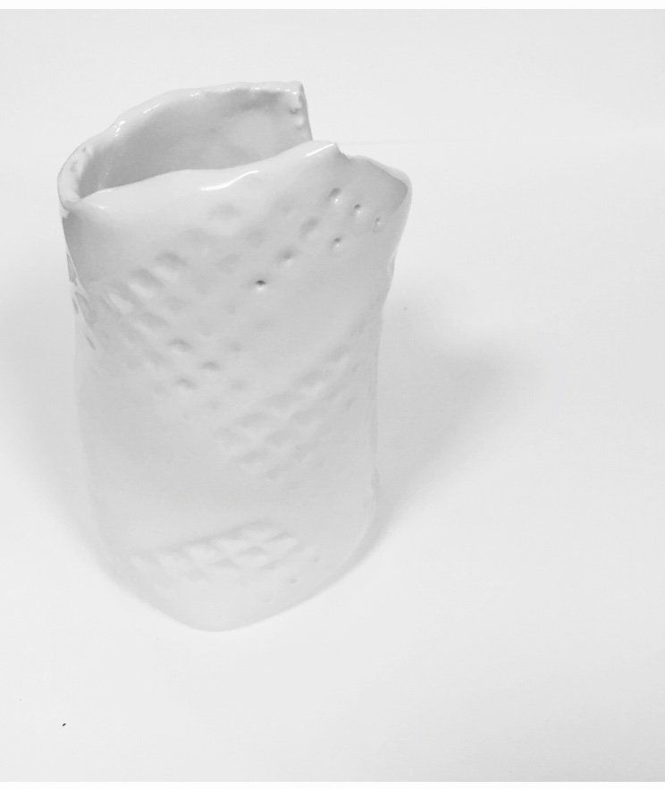 A white vase is sitting on a white surface.