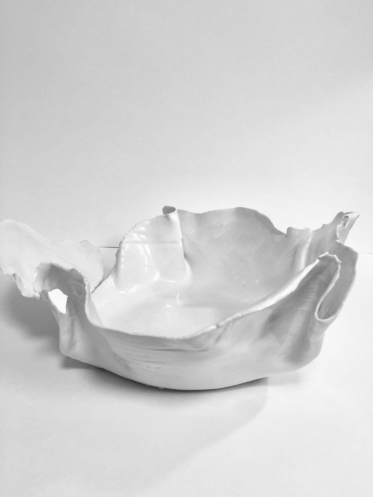 A white bowl with a handle is sitting on a white surface.