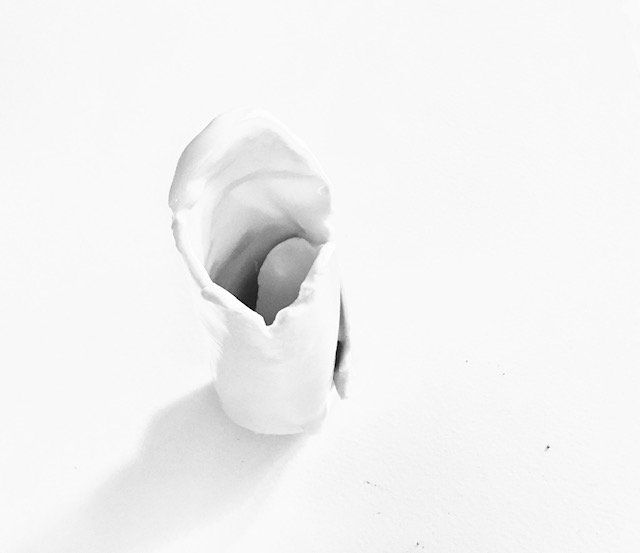 A white vase with a heart in it is sitting on a white surface.