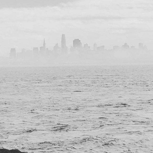 A black and white photo of a city skyline over a body of water.