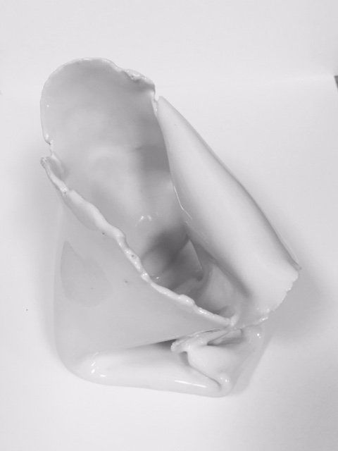 A broken white vase is sitting on a white surface.