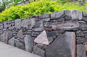 Stone retaining wall with lush green plants on top.