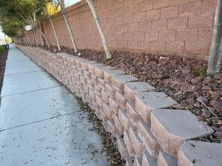 A long, brick retaining wall beside a sidewalk, with mulch and trees.