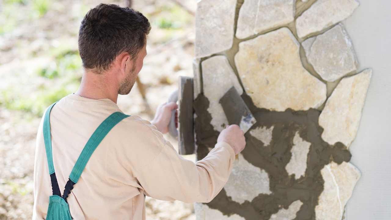 “Hands placing red masonry blocks into fresh mortar for a block and retaining wall build”