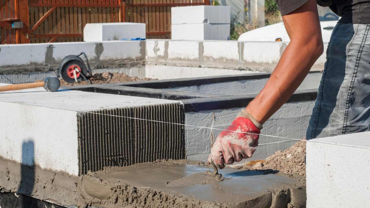 “Close-up of mortar being applied along a concrete block wall during block and retaining wall work”