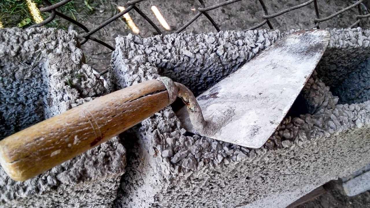 “Close-up of a trowel moving wet mortar for block and retaining wall construction”