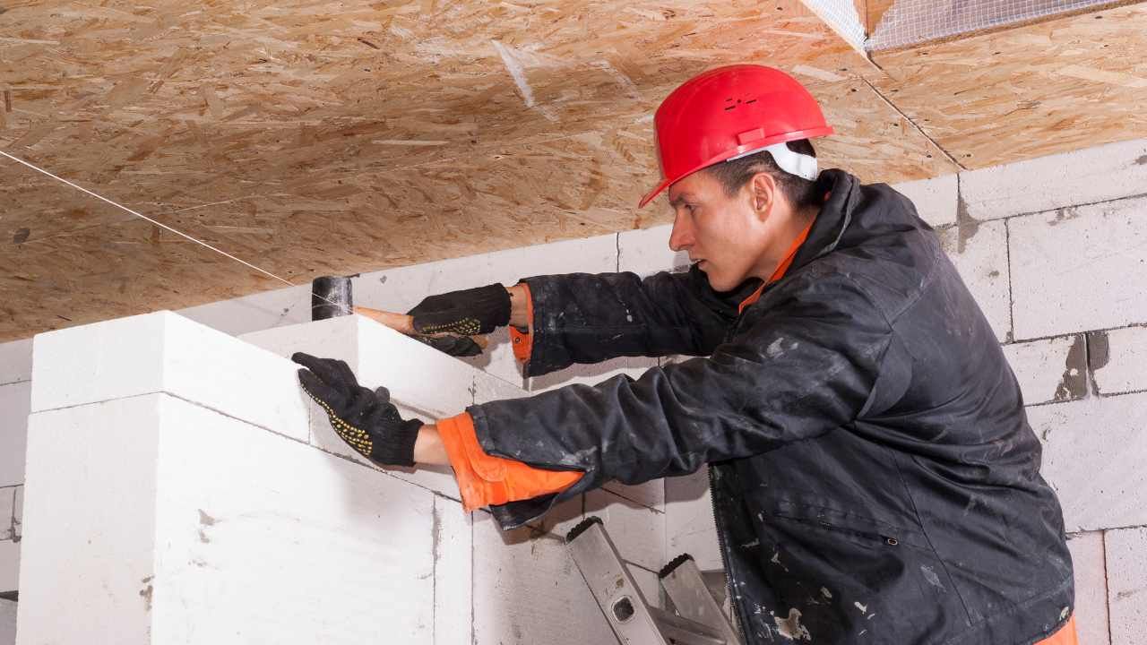 “Worker building a block wall under a covered structure during a block and retaining wall project”