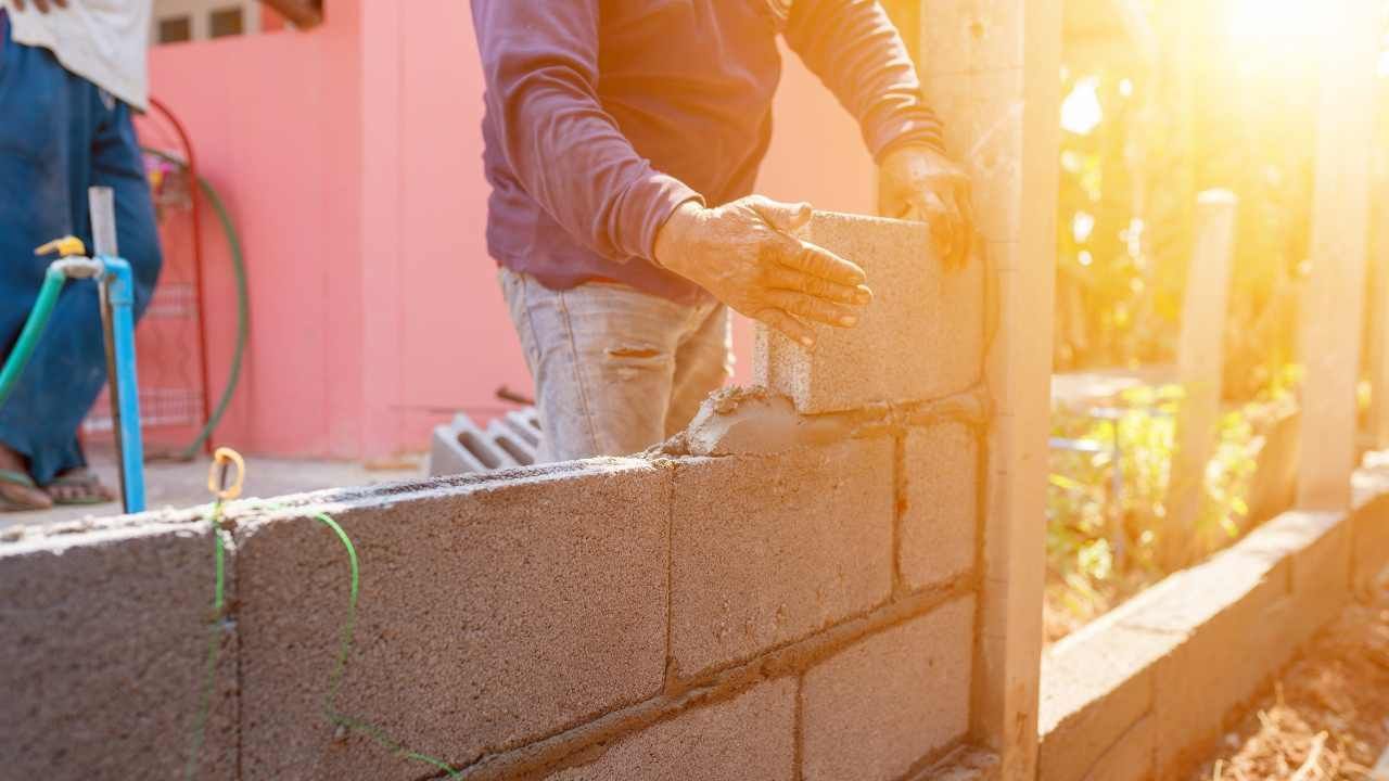 “Worker laying concrete blocks in warm sunlight during block and retaining wall construction”