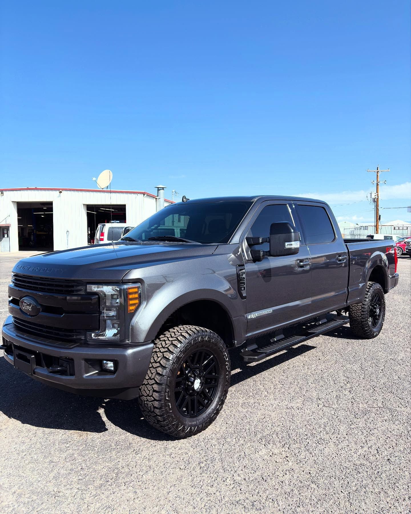 A dark gray Ford F-250 pickup truck with black aftermarket wheels and lifted suspension, parked on a gravel lot.