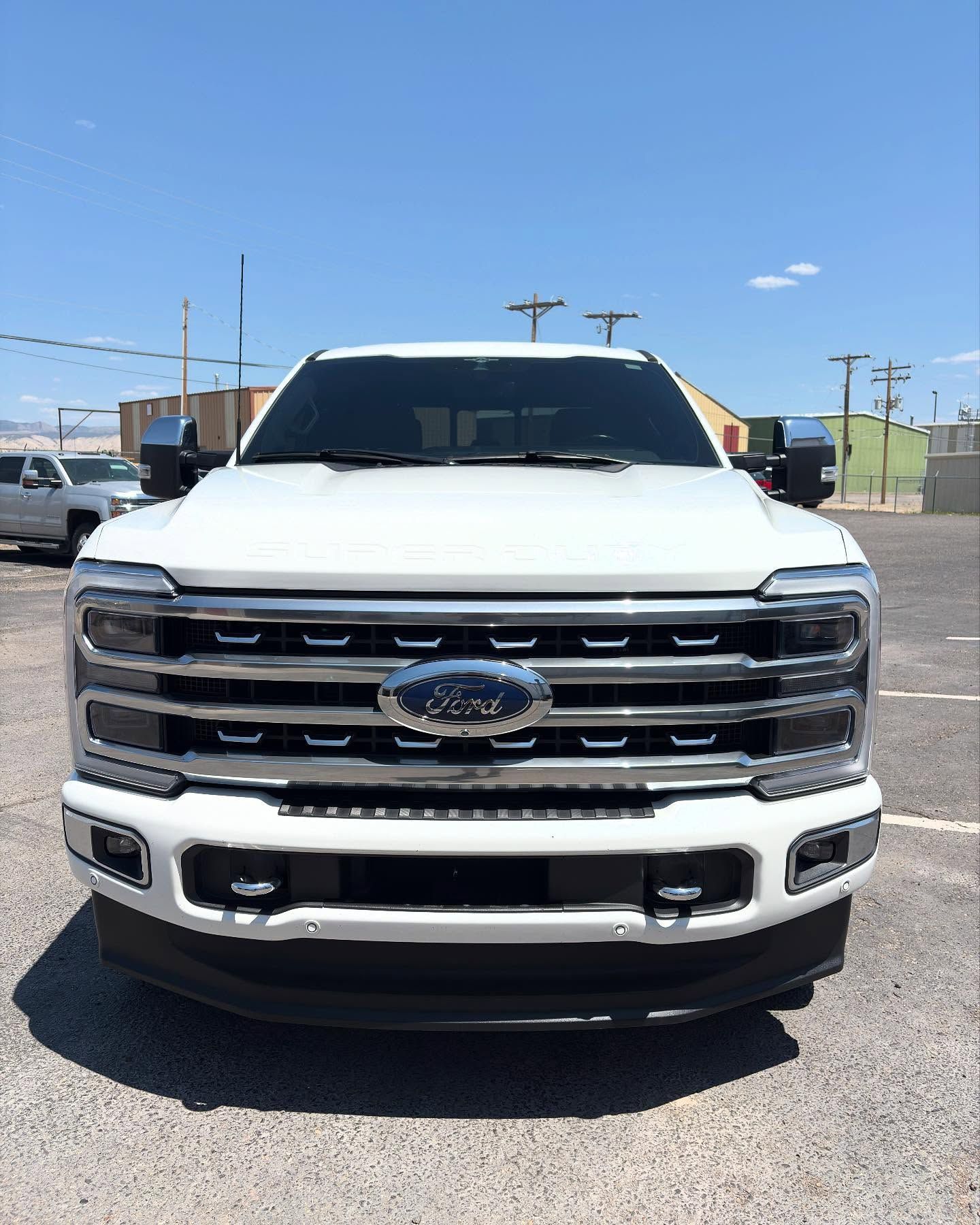 A white Ford Super Duty truck parked outdoors under a clear blue sky, viewed from the front.