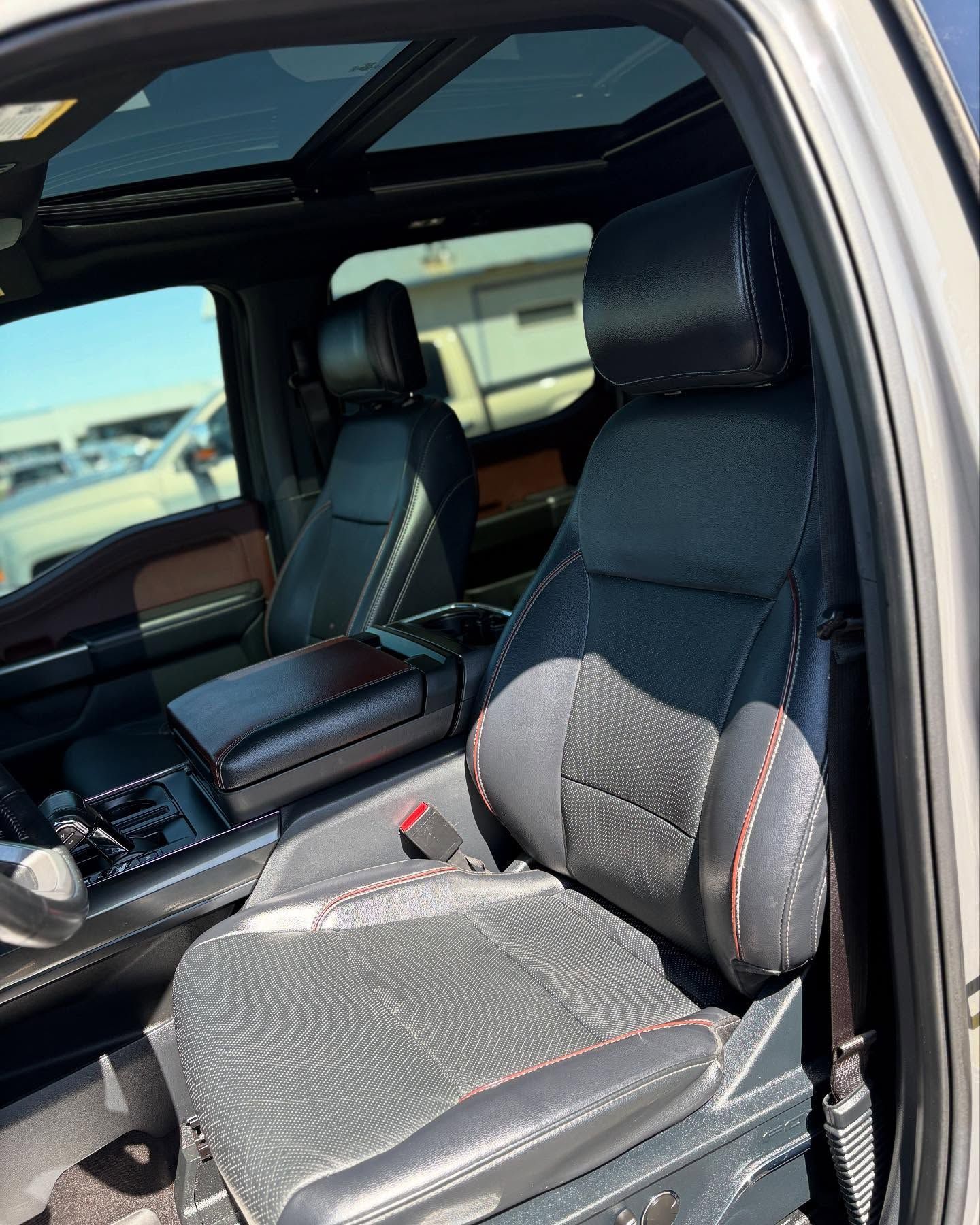 Black leather car interior with red stitching, featuring front bucket seats and a panoramic sunroof.