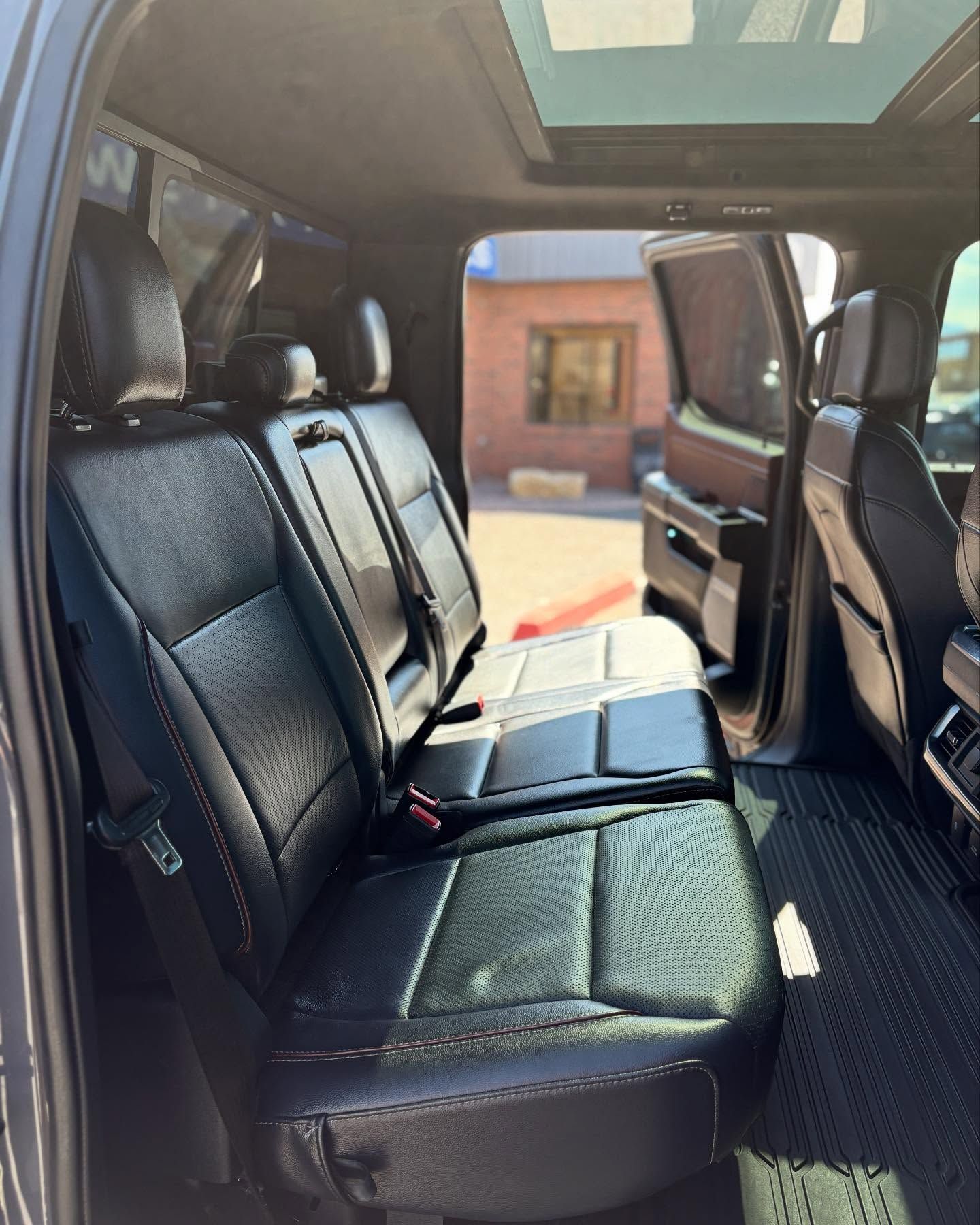 A view of a modern truck's black leather rear seats, floor mats, and sunroof through an open passenger door.