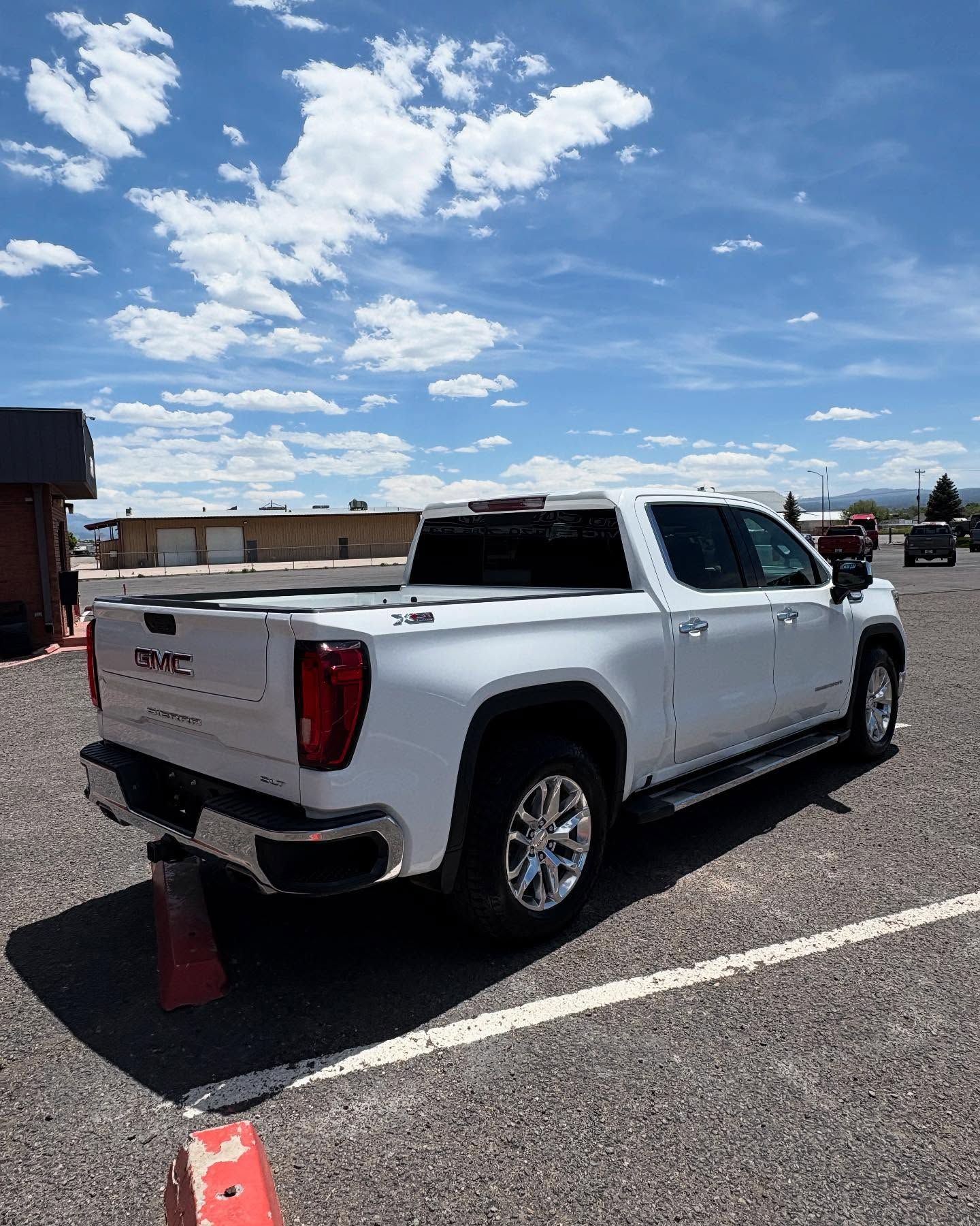 A white GMC pickup truck parked on a gravel lot under a blue sky with scattered clouds.