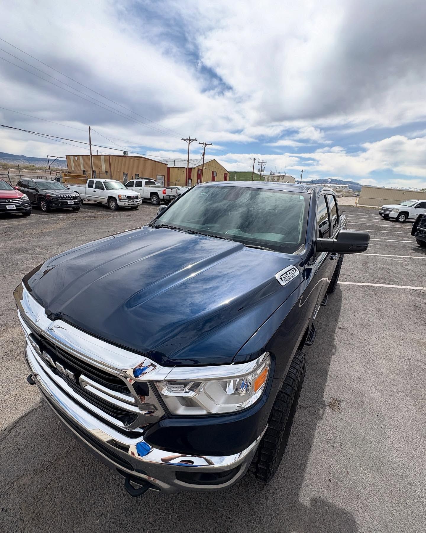 A dark blue Ram pickup truck parked in an outdoor gravel lot under a cloudy sky.