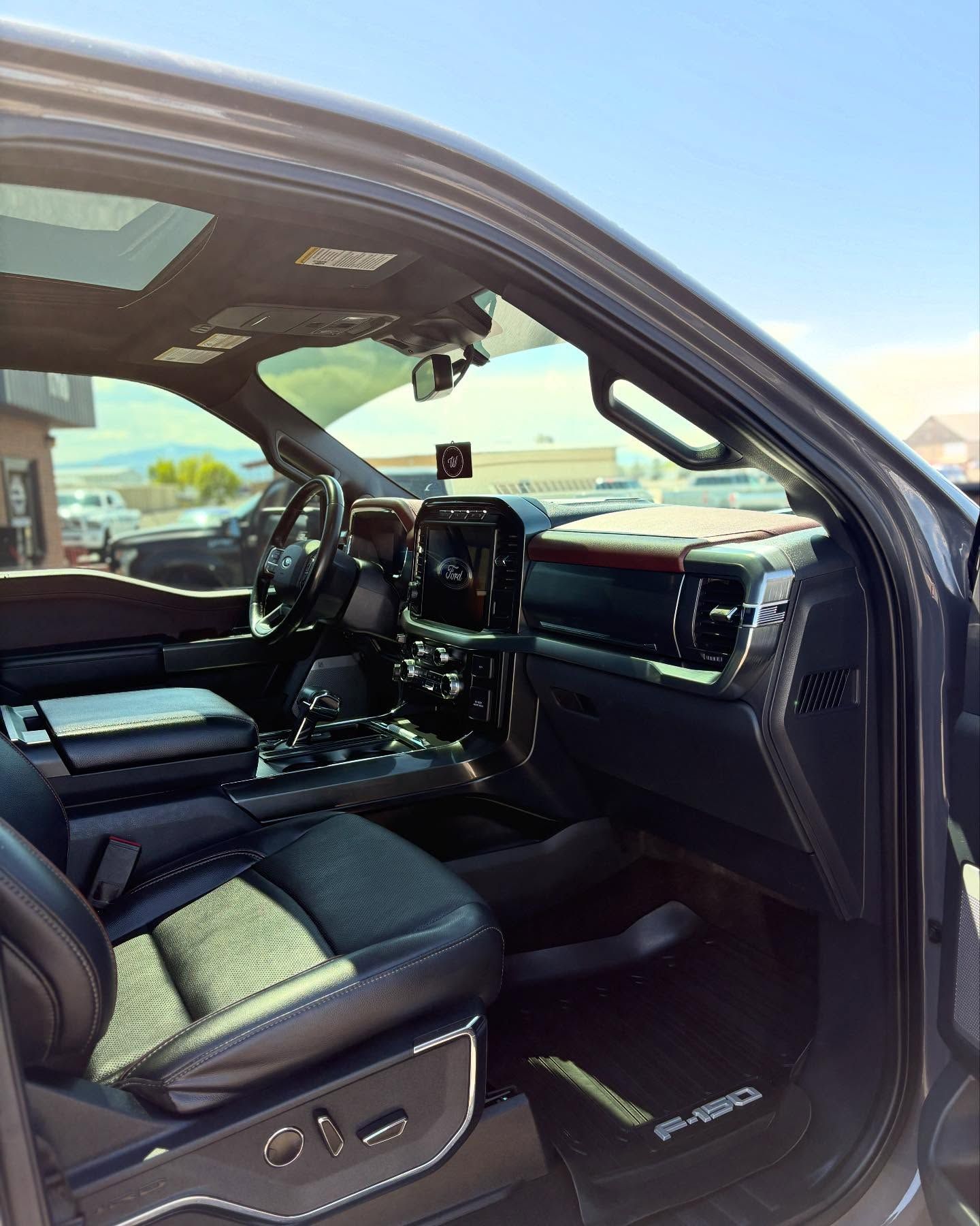 Interior of a modern truck, featuring black leather seats with white stitching, a dark dashboard, and F-150 floor mats.