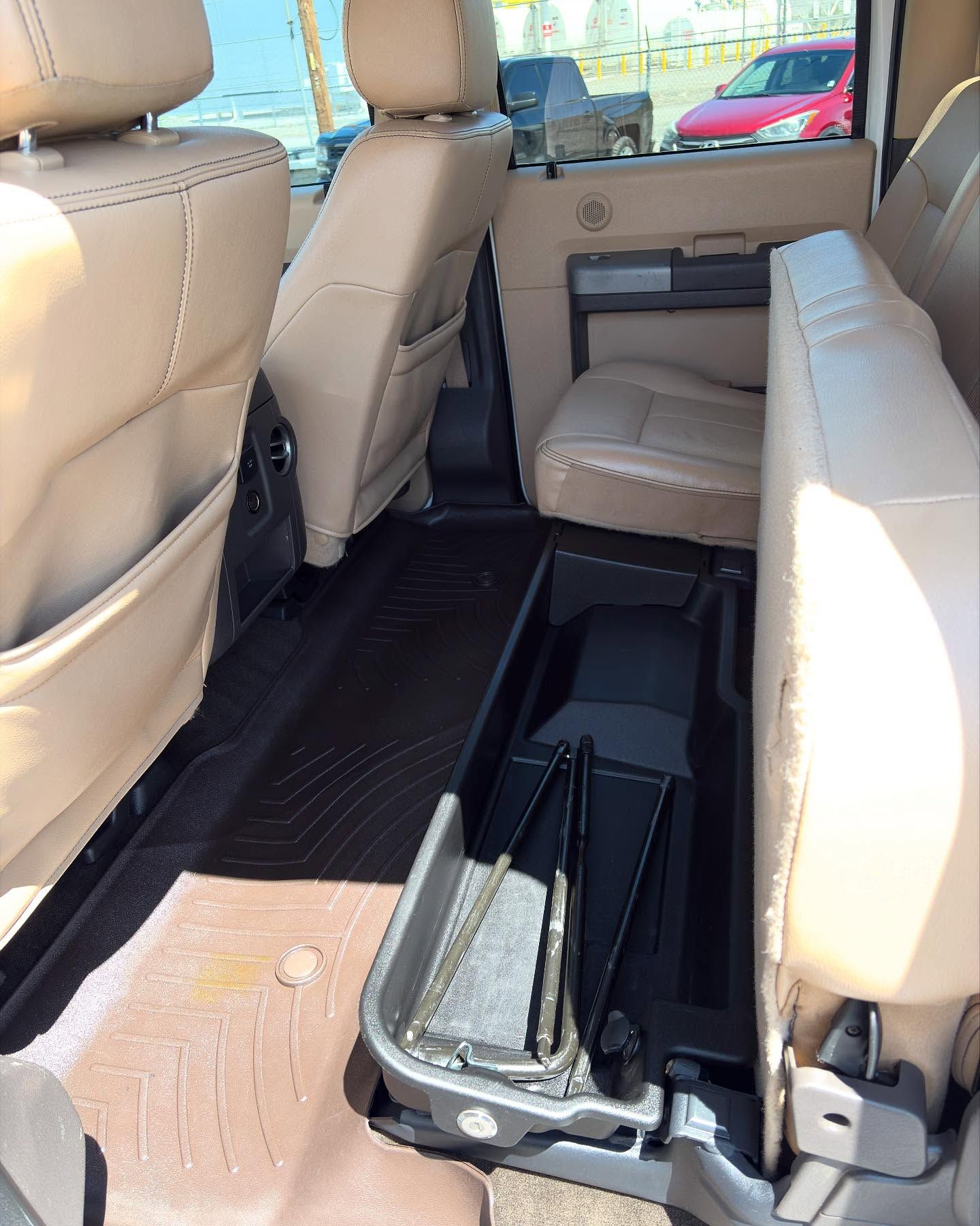 Tan truck interior with folded-up back seats, revealing black floor storage containing tools and a dark floor mat.