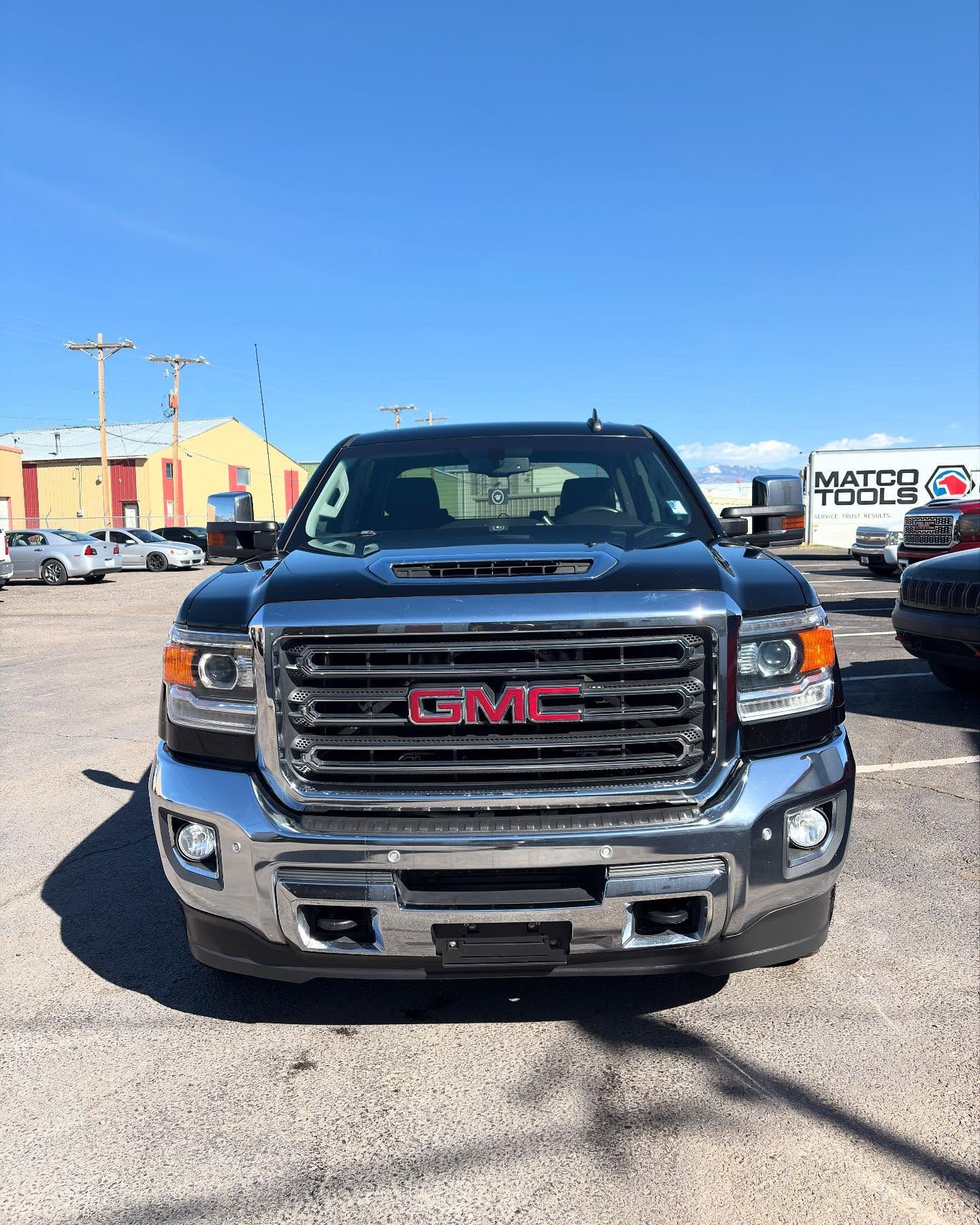 A black GMC Sierra truck parked in a sunny, outdoor gravel lot under a clear blue sky.