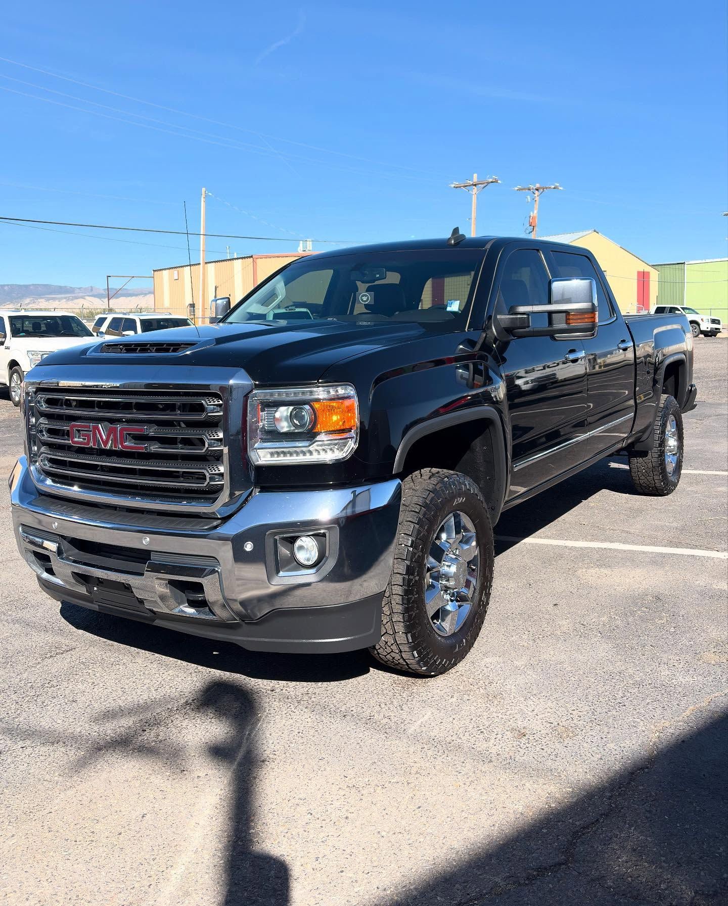 A black GMC Sierra pickup truck parked on a sunny gravel lot with other vehicles in the background.