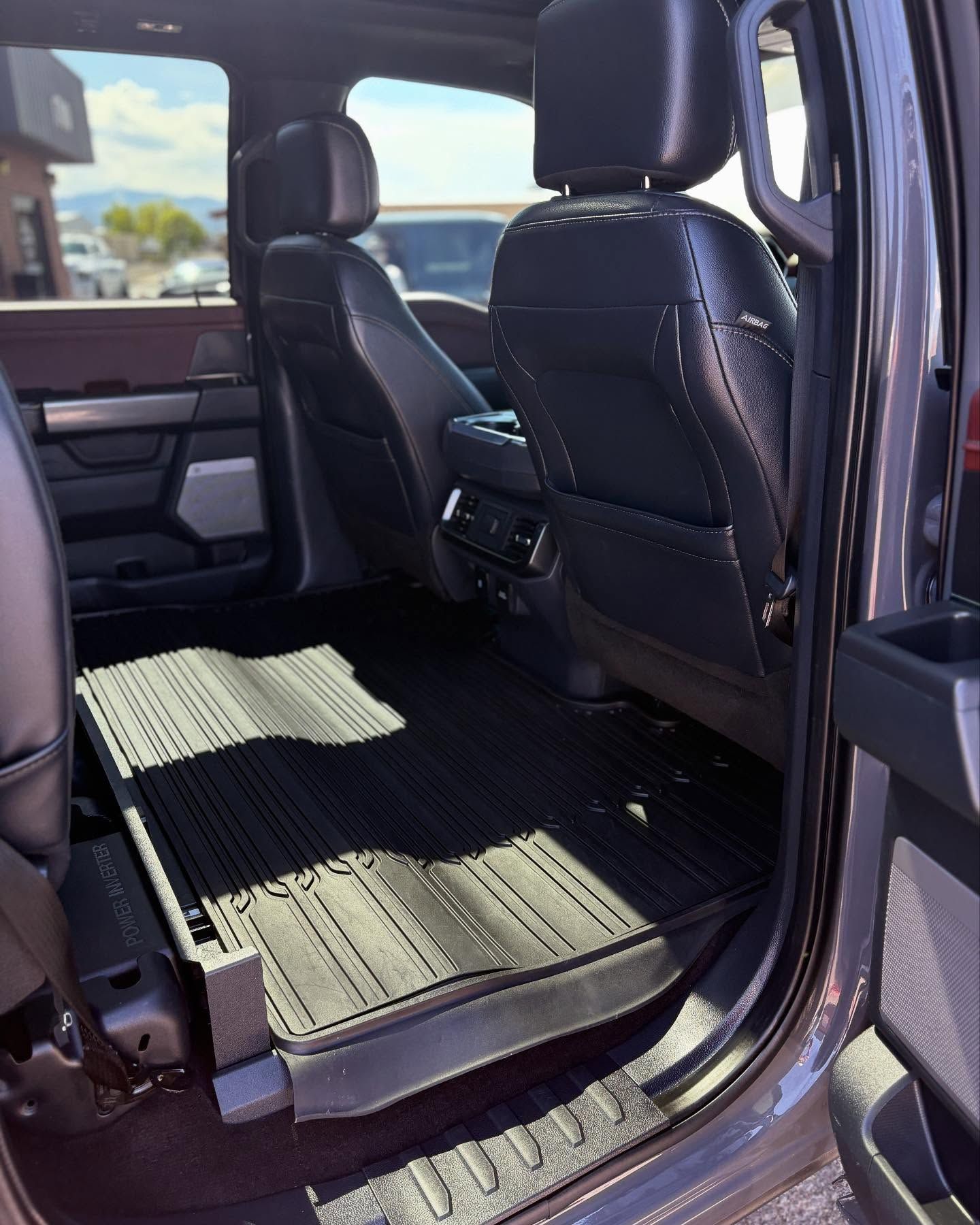 The interior of a vehicle's back seat area featuring black leather seats and fitted, ribbed black rubber floor mats.