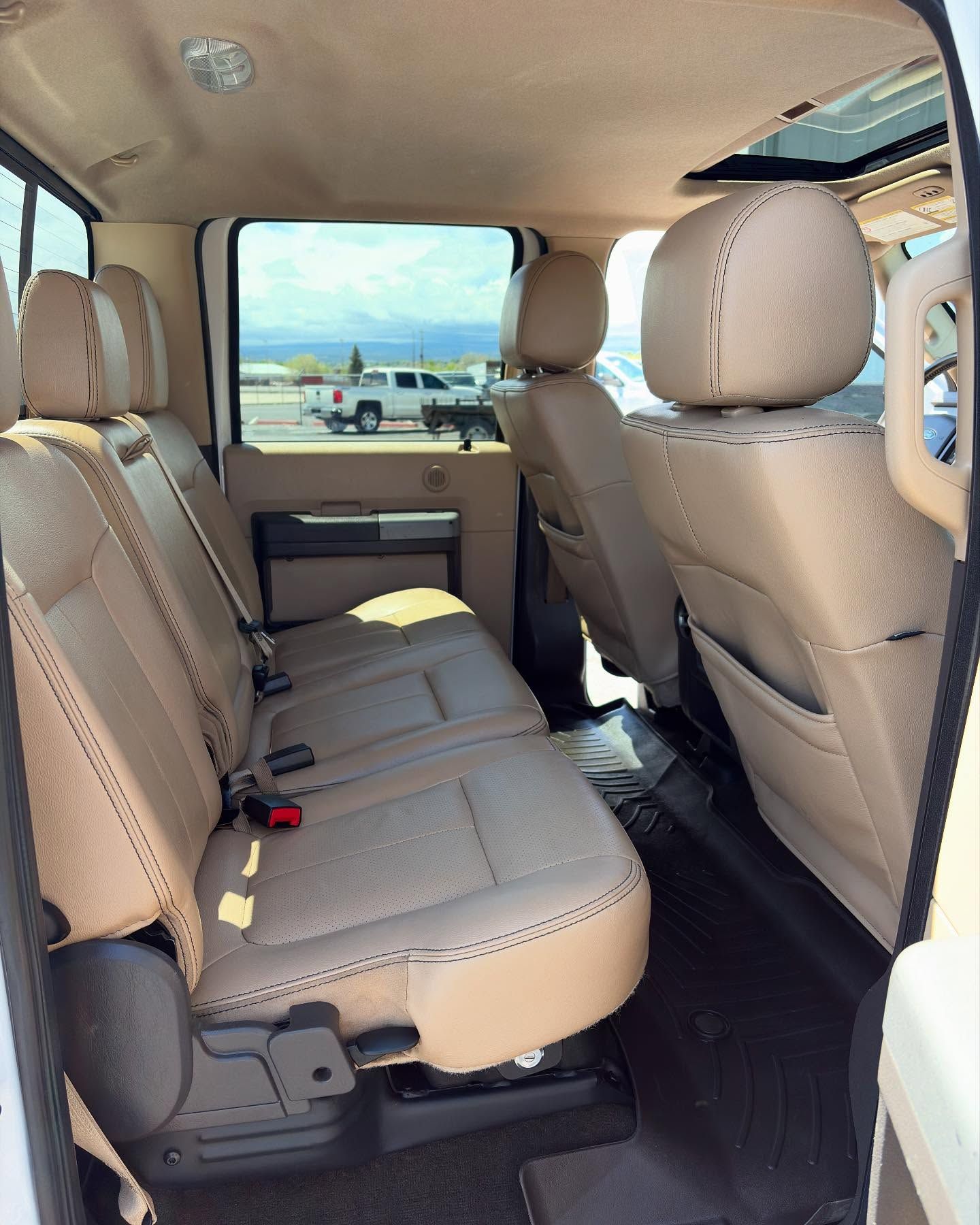 The interior view of a truck’s back cabin, featuring beige leather bench seating and black floor mats.