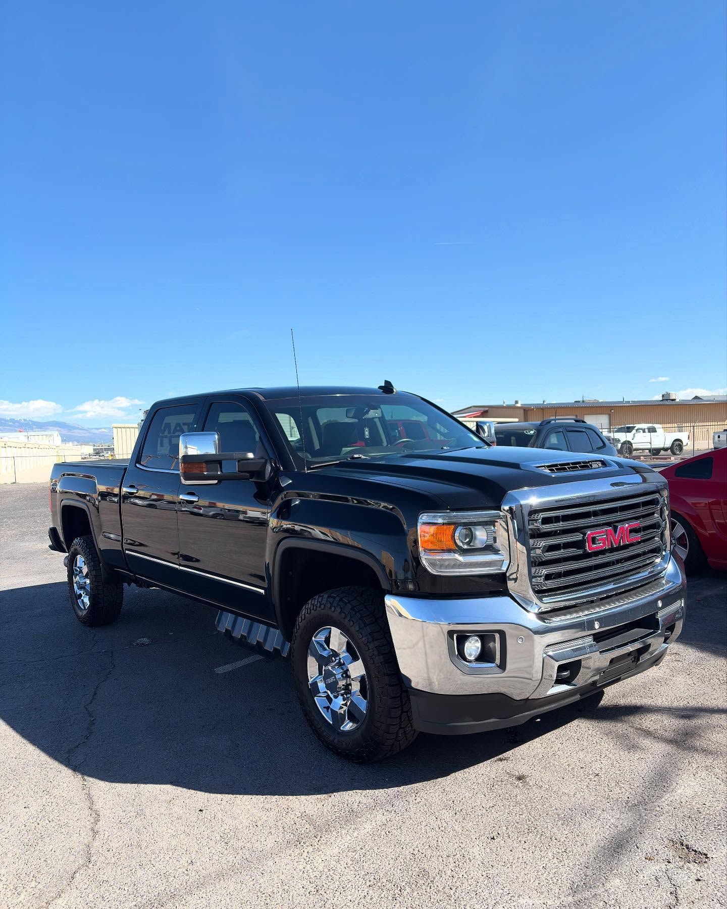 A black GMC Sierra pickup truck parked on an asphalt lot under a clear blue sky.