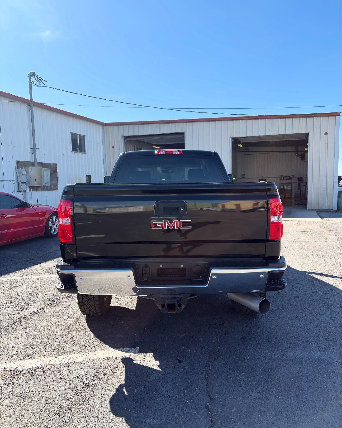 A black GMC pickup truck parked in front of a metal warehouse building on a sunny day.