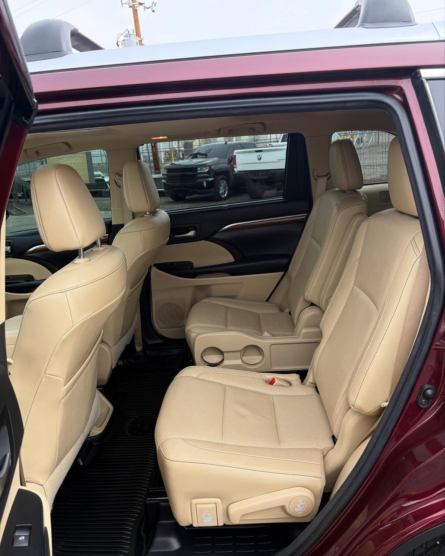 The interior of a maroon SUV showing rows of tan leather captain's chairs and back seating with black floor mats.