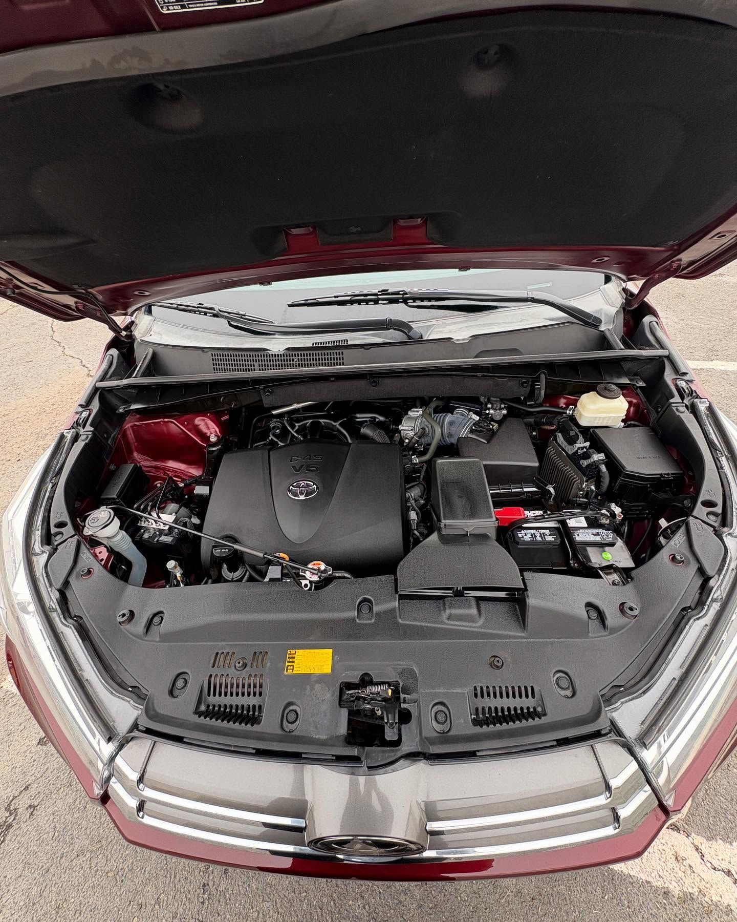 The open hood of a maroon car reveals a clean, dark engine bay, showing the engine cover and various components.