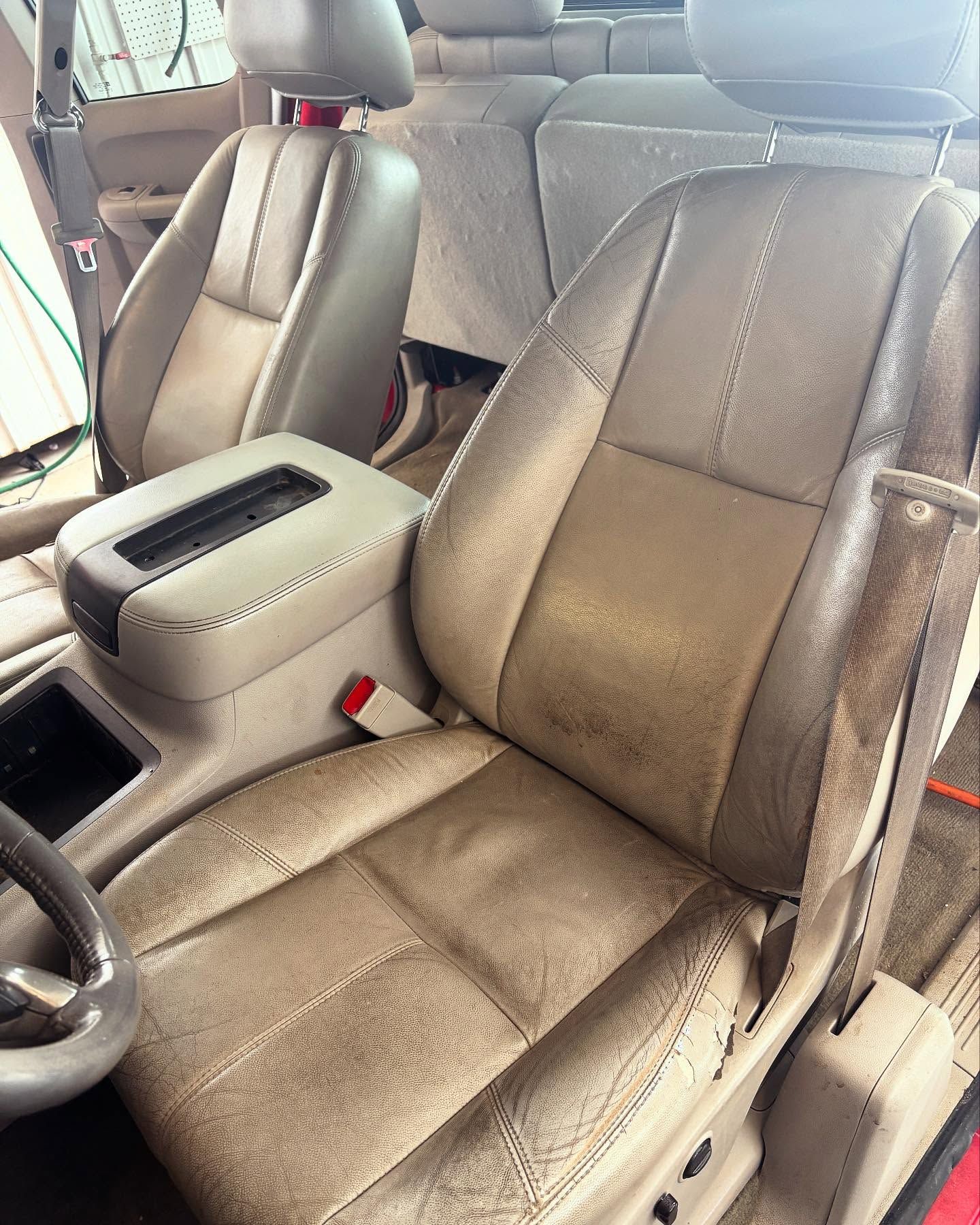 Beige car interior featuring a worn leather front bucket seat, headrest, and center console.