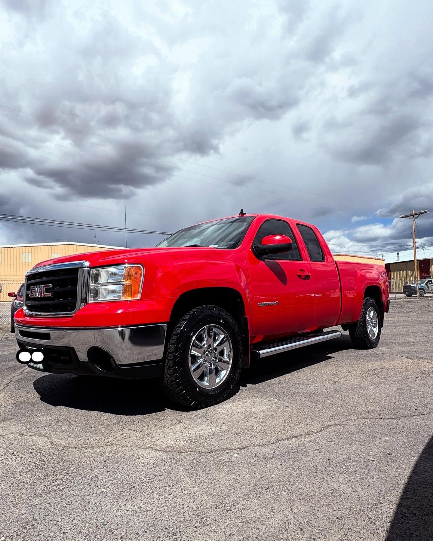 A bright red GMC pickup truck parked on a gravel lot under a cloudy sky.