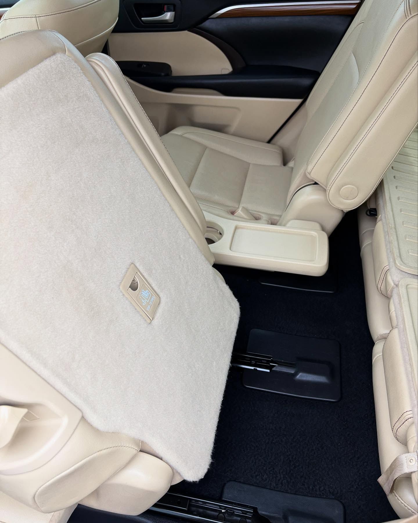 A view of a vehicle's interior showing folded beige seats and a small built-in table between them over black carpet.