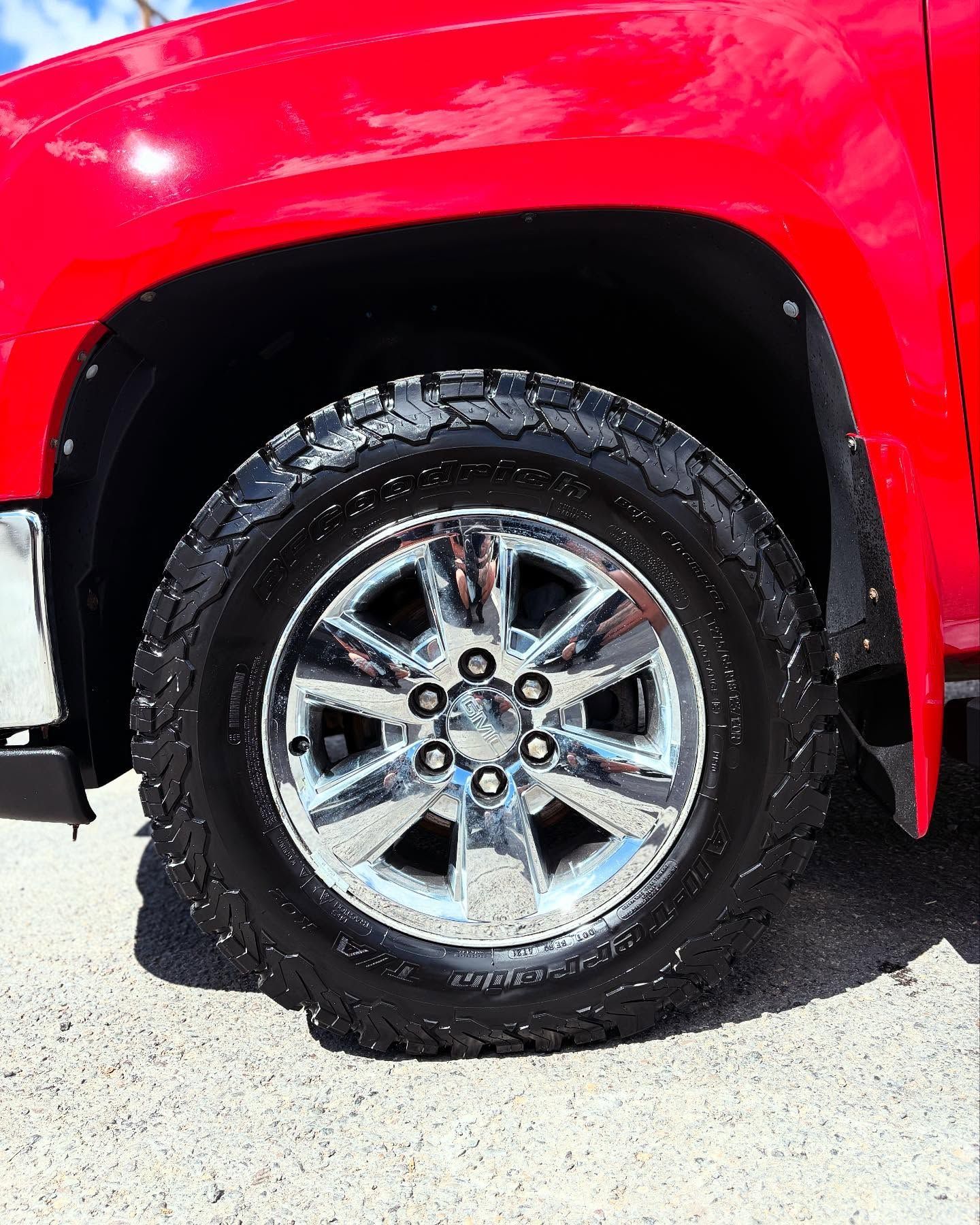 A close-up shot of a chrome six-spoke wheel with an all-terrain tire on a bright red truck fender.