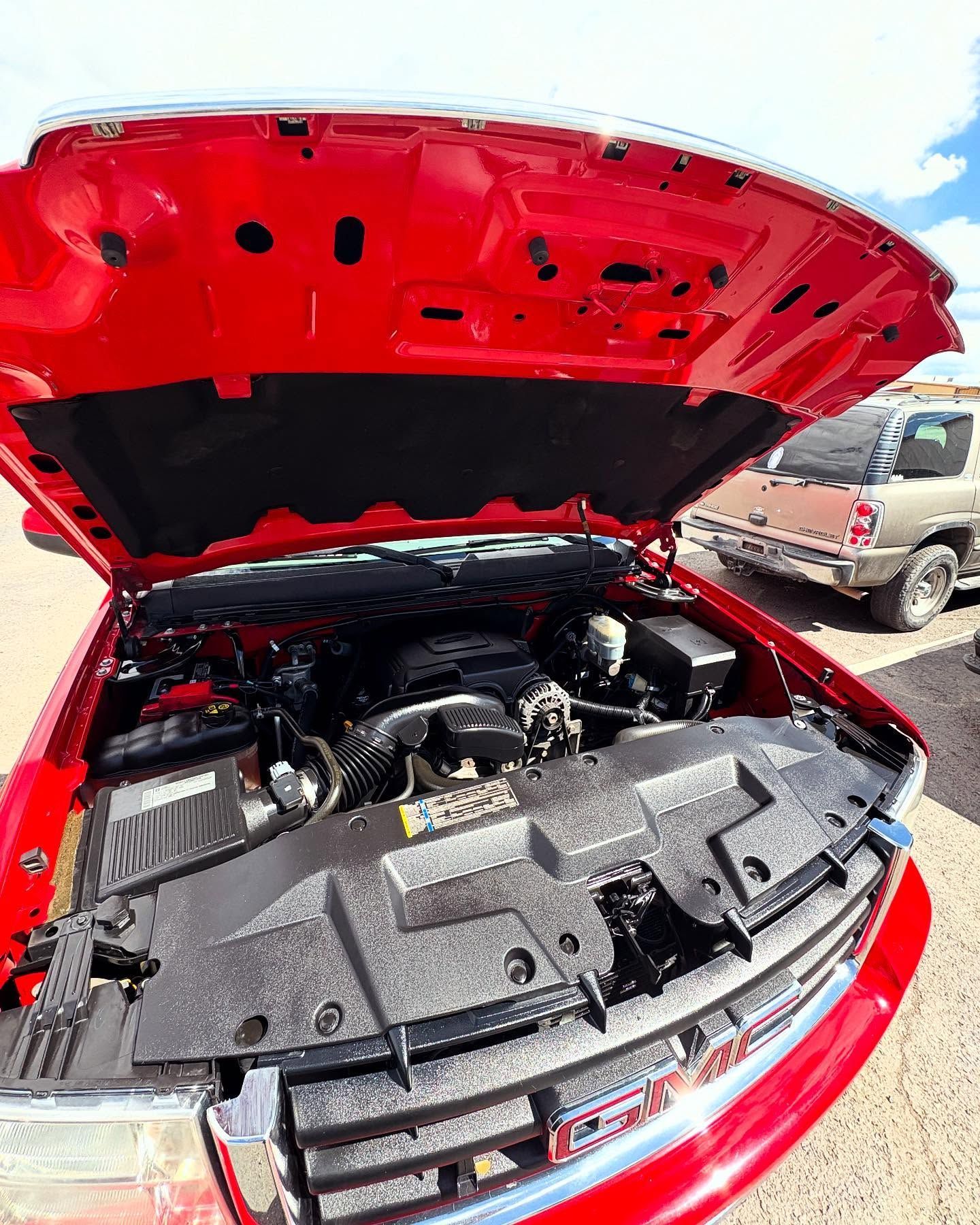An open hood of a bright red truck, showing the engine compartment and a radiator support cover.
