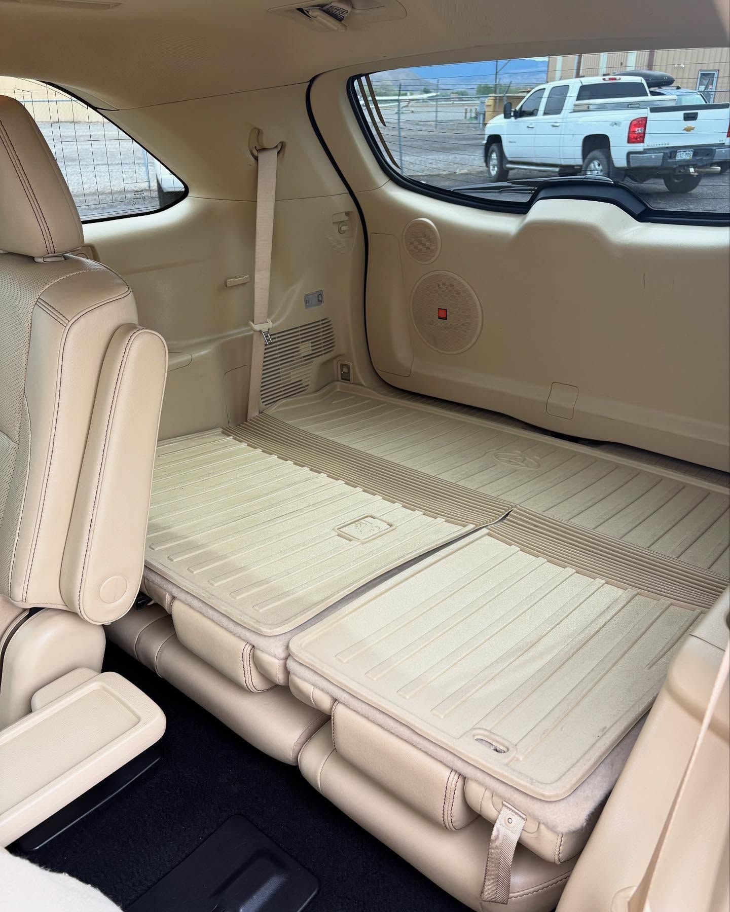 Tan-colored interior of a vehicle with folded-down rear seats, showing a flat cargo area and a view of a truck outside.