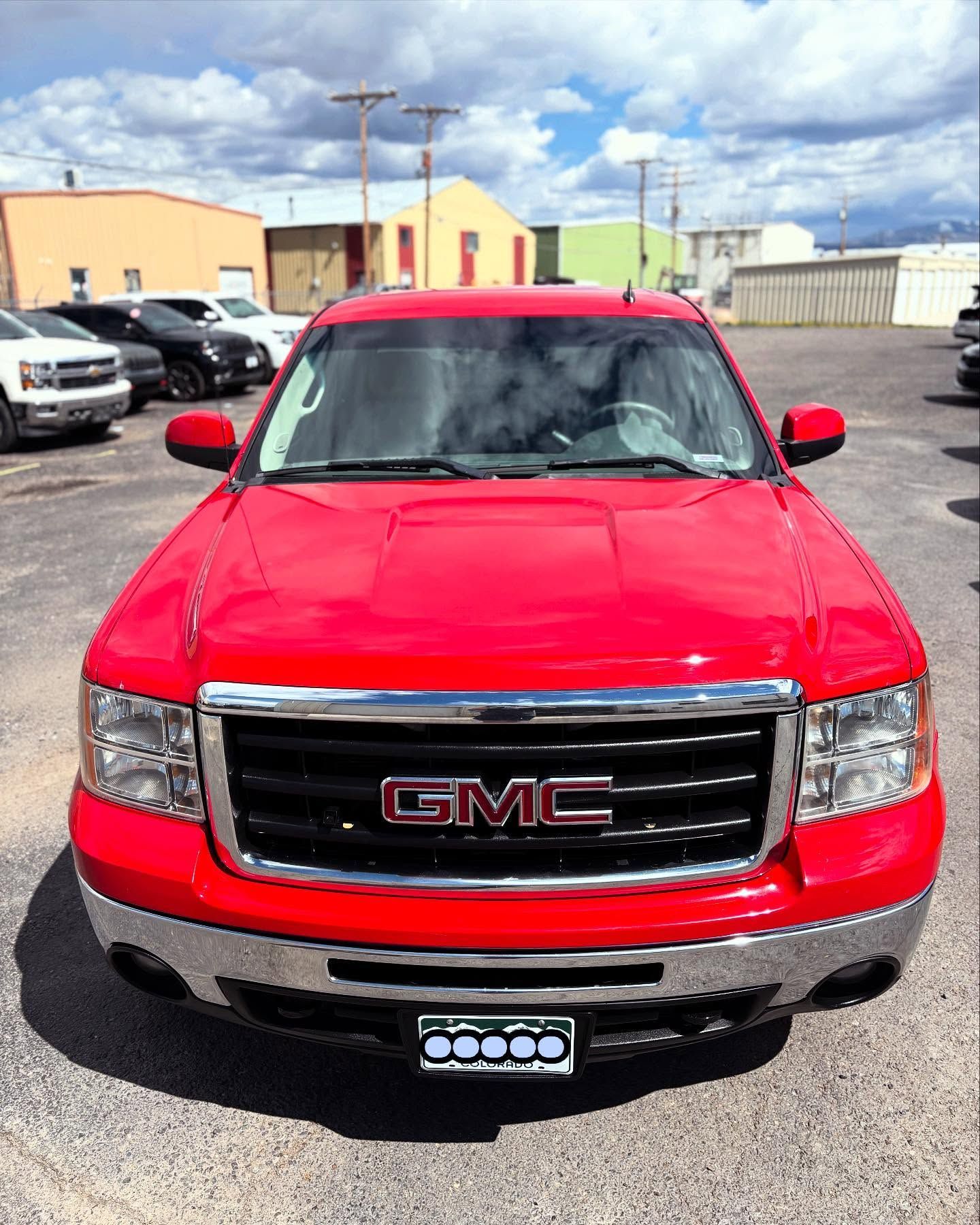 A bright red GMC pickup truck parked in an outdoor lot during the day.
