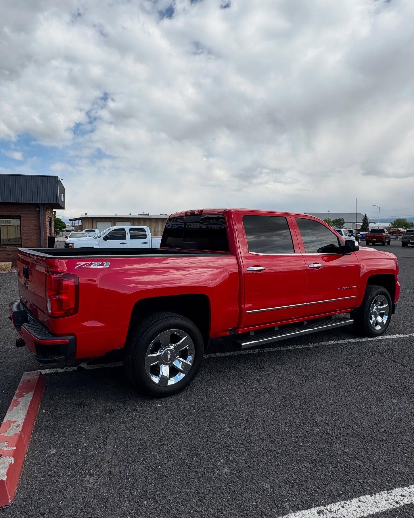 A red Chevrolet Silverado pickup truck parked in a gravel lot under a cloudy sky.